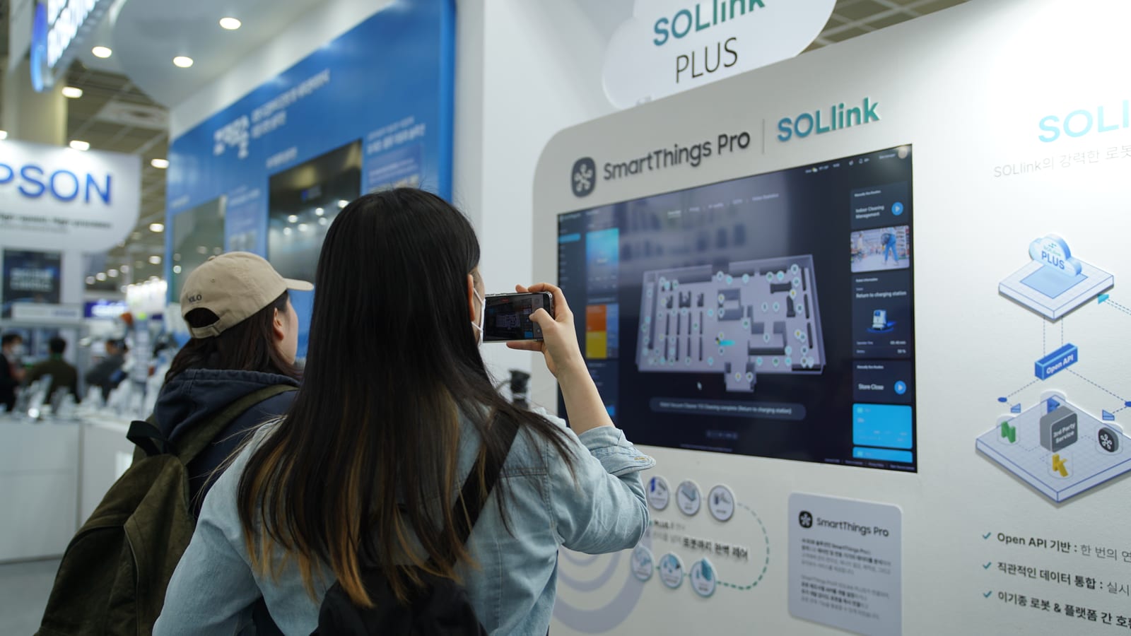 AW 2025 빅웨이브로보틱스 부스. SmartThings Pro와 SOLlink 로고 아래 화면에 매장 3D 맵과 로봇 상태가 표시되어 있고, 관람객이 사진을 찍고 있다.