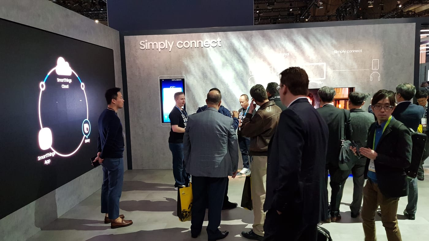 CES 2018 삼성전자 부스의 'Simply connect' 전시 벽면. 왼쪽 대형 화면에 SmartThings Cloud·App·Bixby를 잇는 원형 도식이 있고, 관람객들이 데모를 보고 있다.